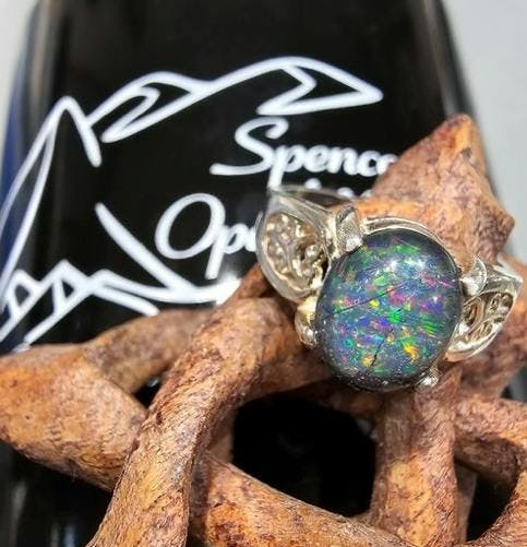 Ring with opal center piece on piece of wood, with something in the back that says "Spencer Opal Mines".