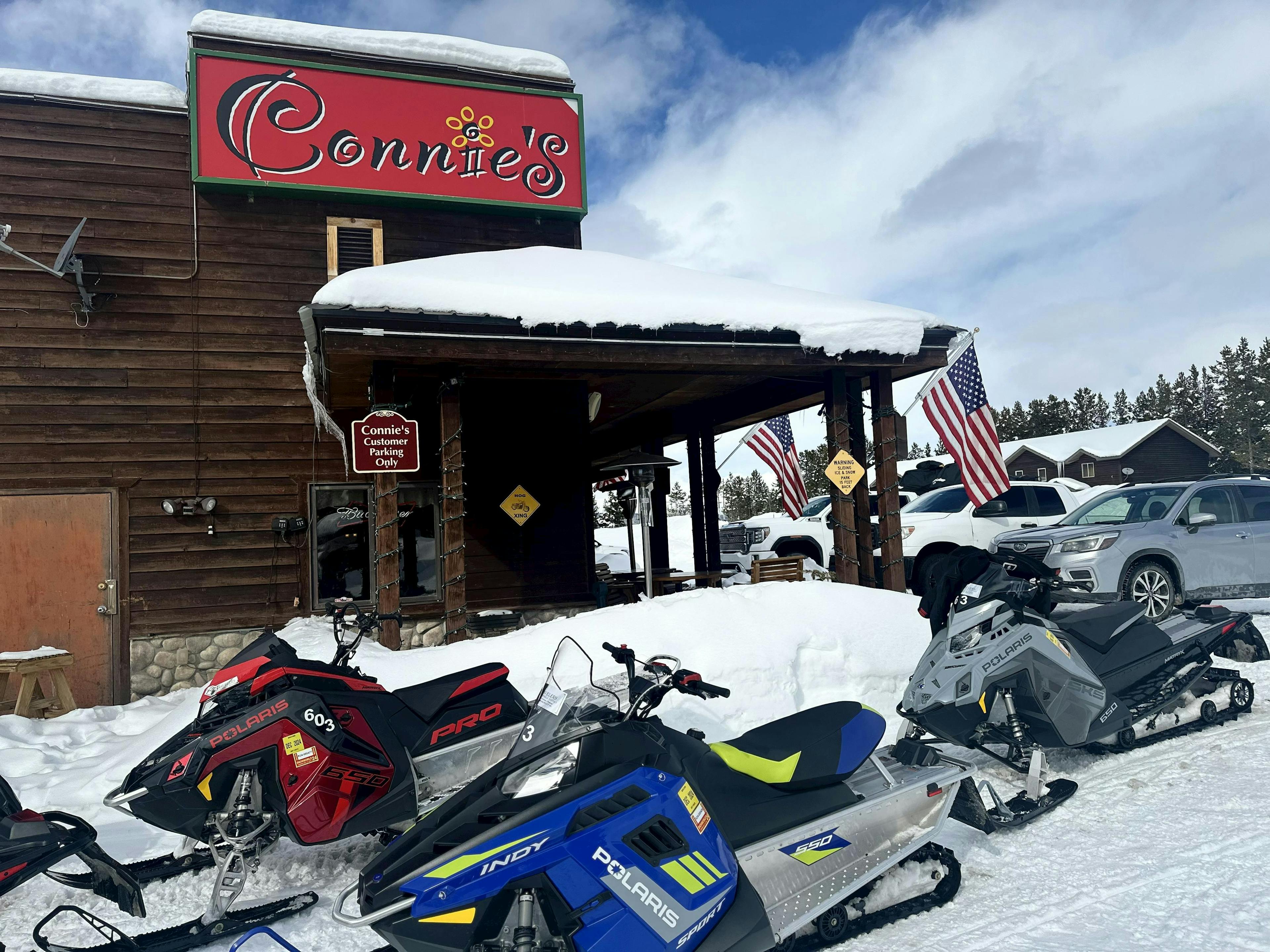 Connie's Restaurant sign with snow machines parked in front in Island Park, Idaho. 